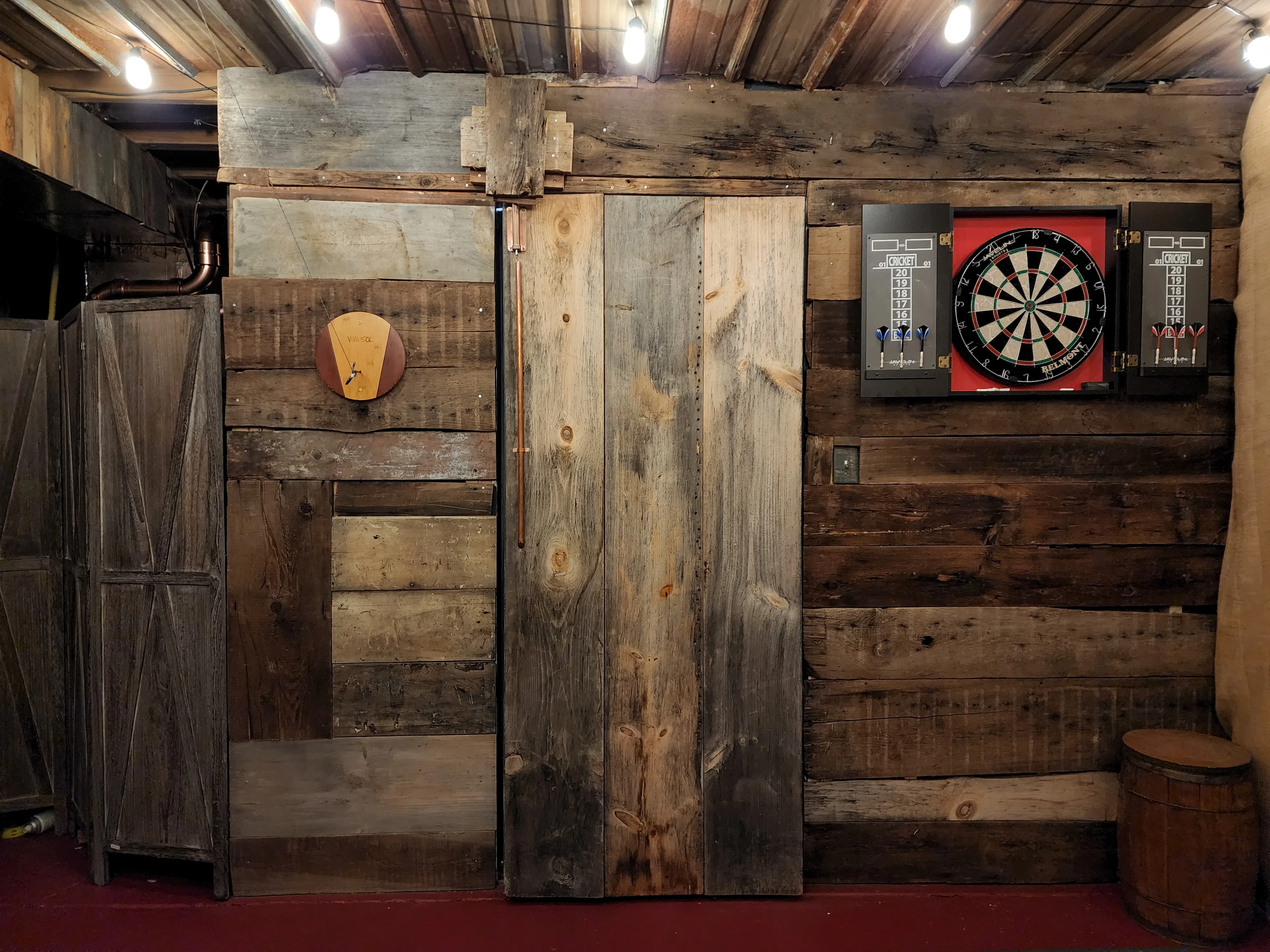 Rustic wall with 100 year old beams. Secret door bookcase back with weathered wood. Dartboard and patio lights on corrugated metal